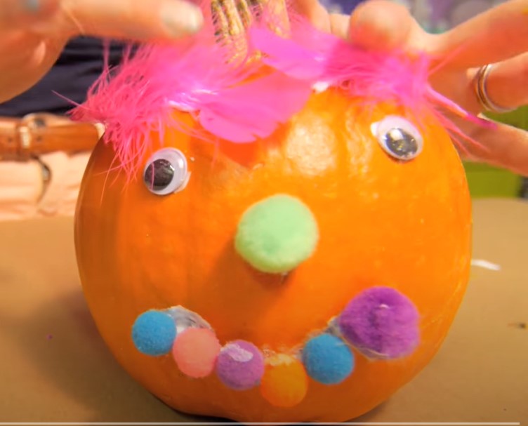 Kids Pumpkin Party - pumpkin example featuring googly eyes, pompom balls for the mouth and noes, and bright pink feathers for hair.